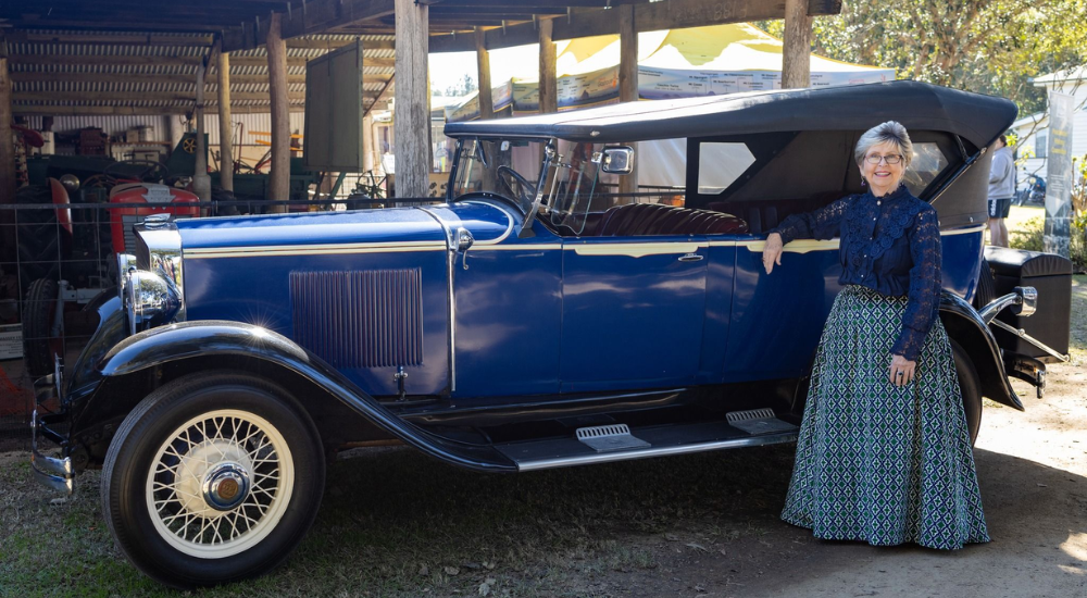 Local in a heritage dress posing in front of a vintage car for Heritage Day